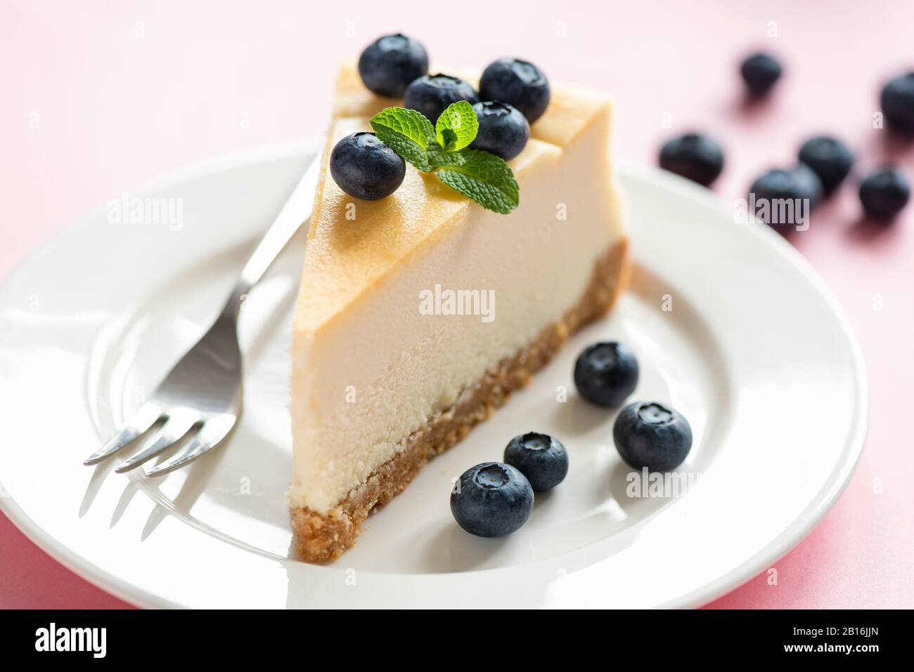 Classical Cheesecake Slice Served With Fresh Blueberries And Mint Leaf On White Plate, Pink Background. Tasty Sweet Dessert Food. Creamy Cake Stock Photo