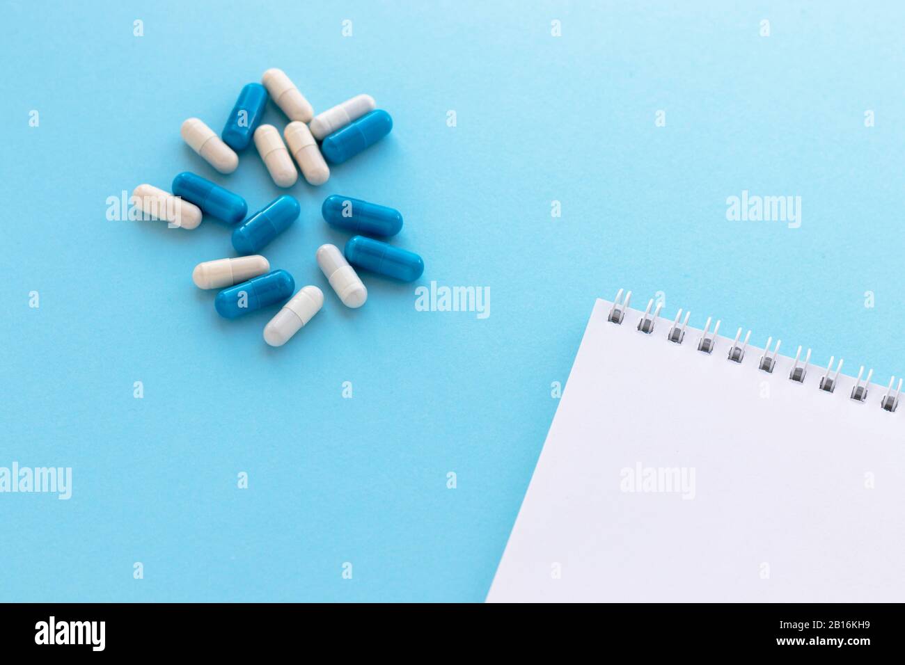 Stack of capsules and blank notepad isolated on light blue background ...