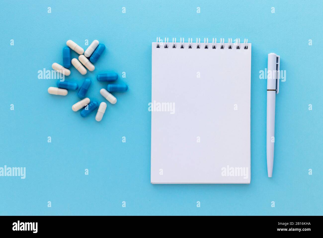 Stack of capsules, blank notepad and pen isolated on light blue ...