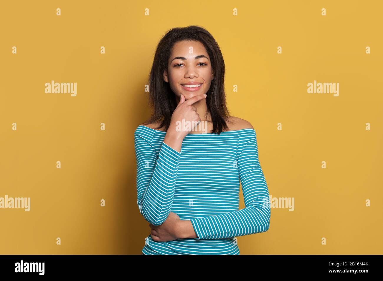 Cute smart mixed race ethnicity black woman in blue shirt thinking on colorful yellow background Stock Photo