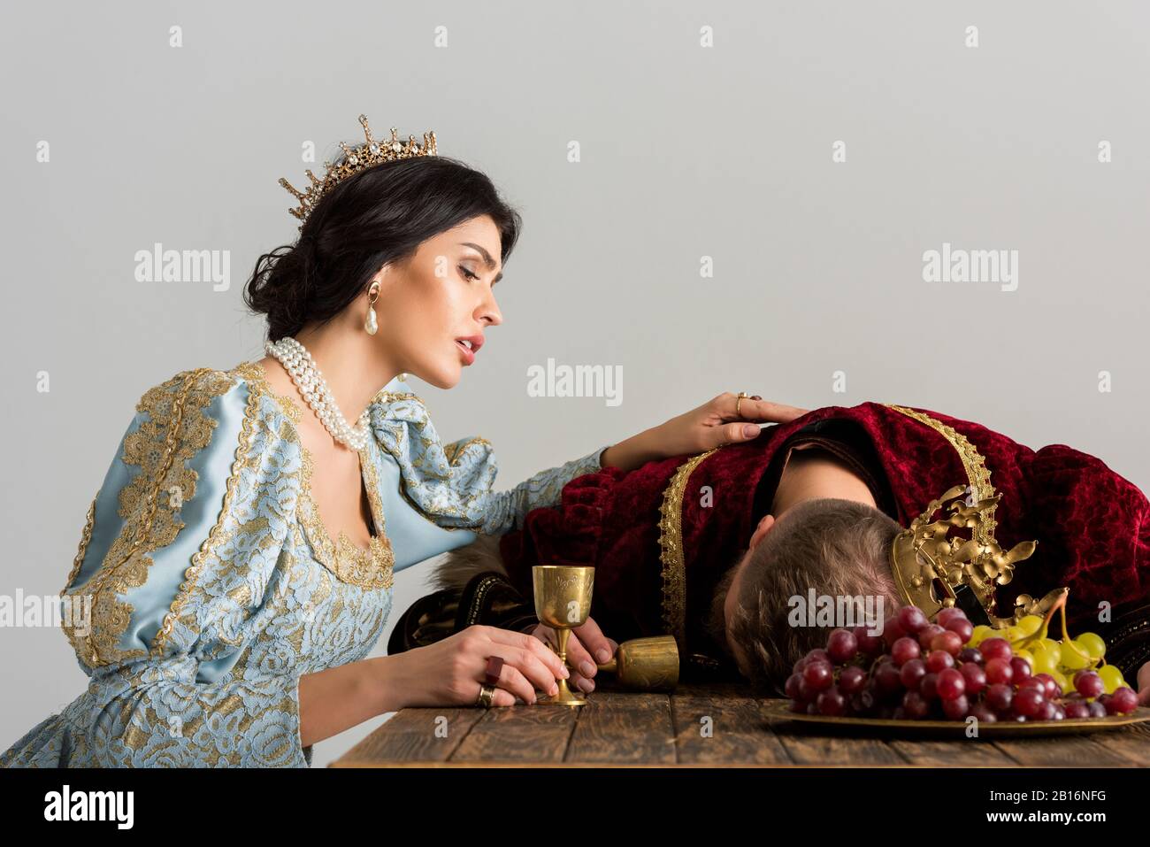 sad queen with crown looking at killed king isolated on grey Stock Photo