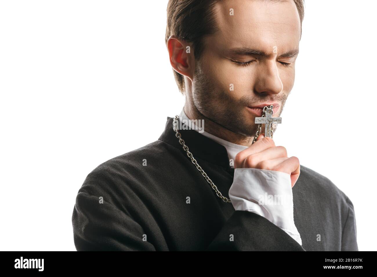 young, serious catholic priest kissing holy cross with closed eyes