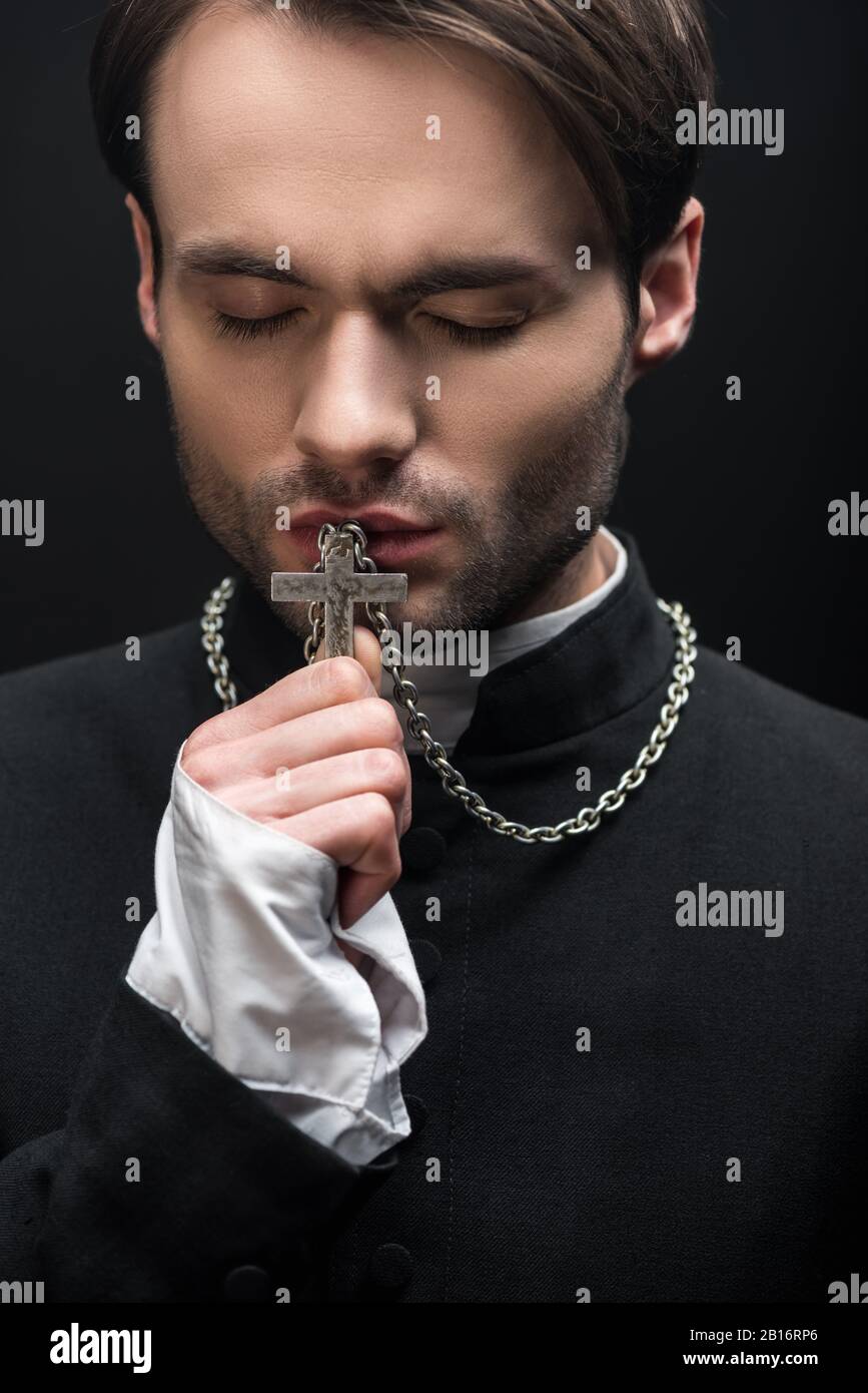 young thoughtful catholic priest kissing cross with closed eyes