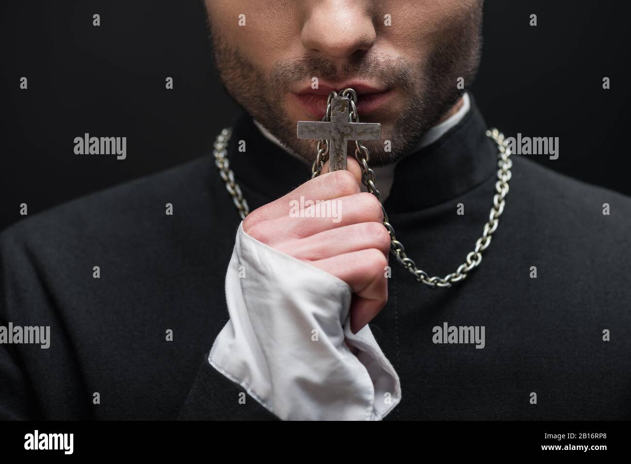 cropped view of catholic priest kissing silver cross on his necklace
