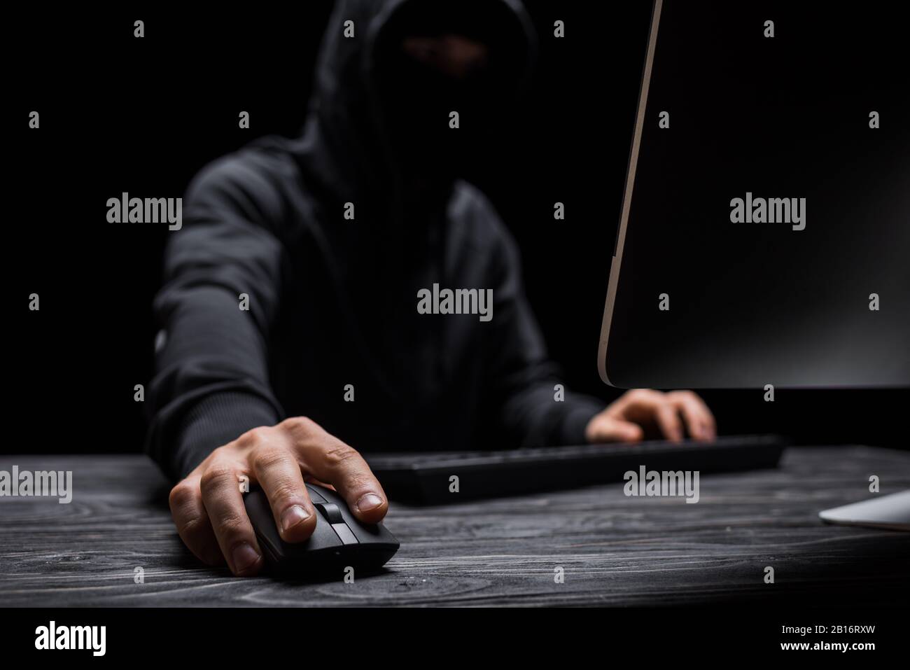 selective focus of computer mouse in hand on hacker isolated on black Stock Photo