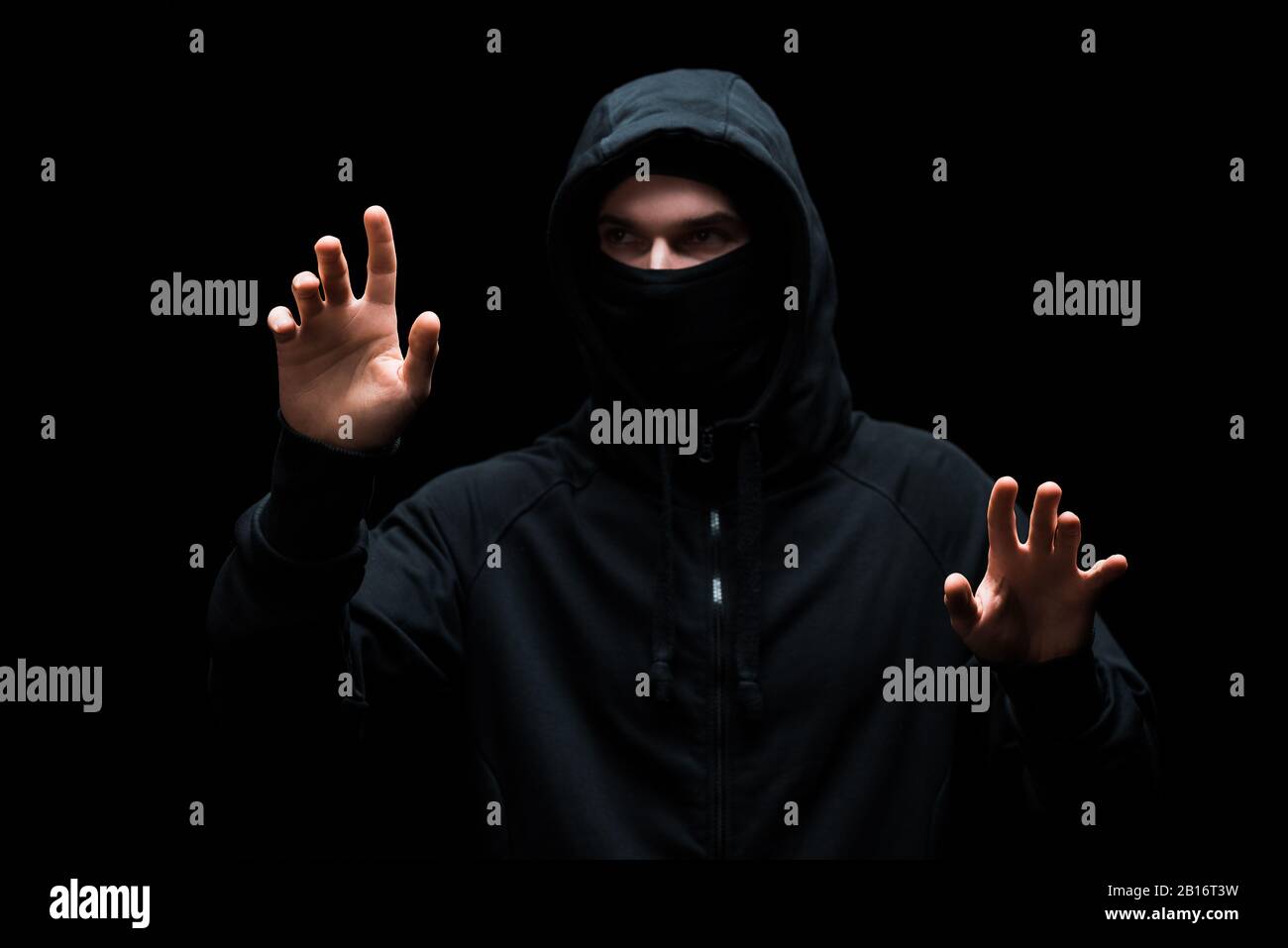 anonymous hacker in hood gesturing isolated on black Stock Photo