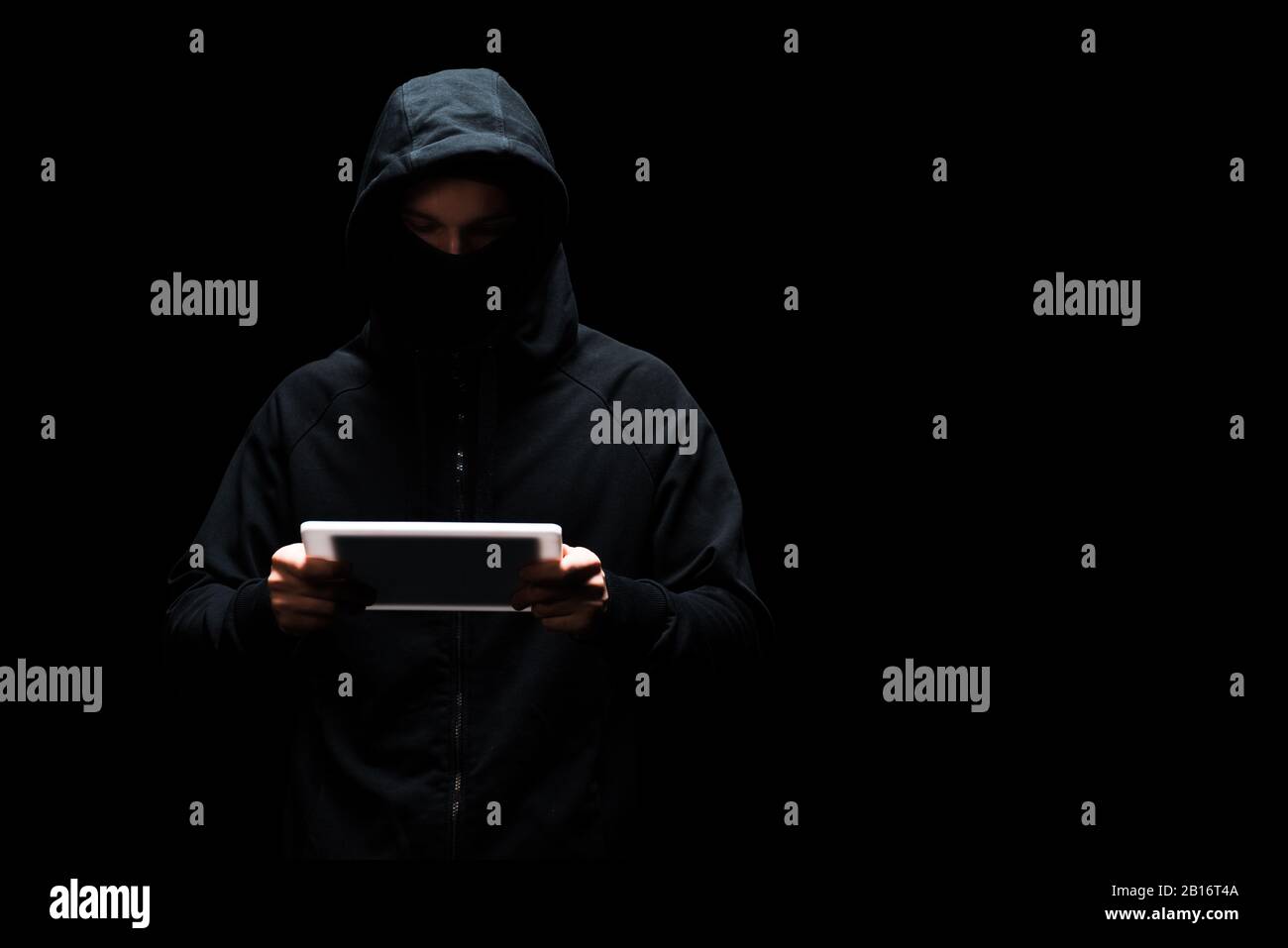 anonymous hacker in hood and mask using digital tablet isolated on black Stock Photo