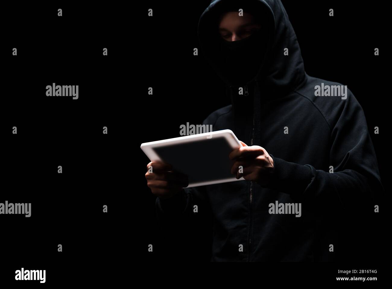 anonymous hacker in hood using digital tablet isolated on black Stock Photo