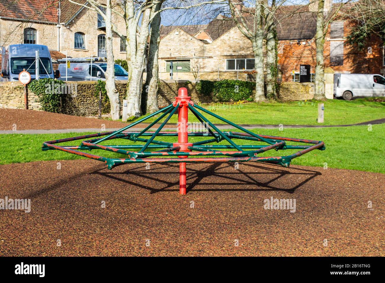 A vintage green and red playground roundabout in the style of a basic hexagonal frame like a spiderweb located at the recreation ground in the village Stock Photo