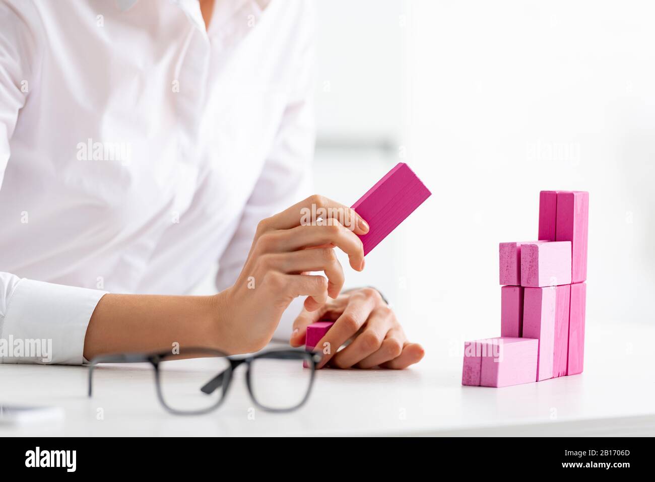 Selective focus of businesswoman stacking marketing pyramid from pink blocks wood game on table Stock Photo