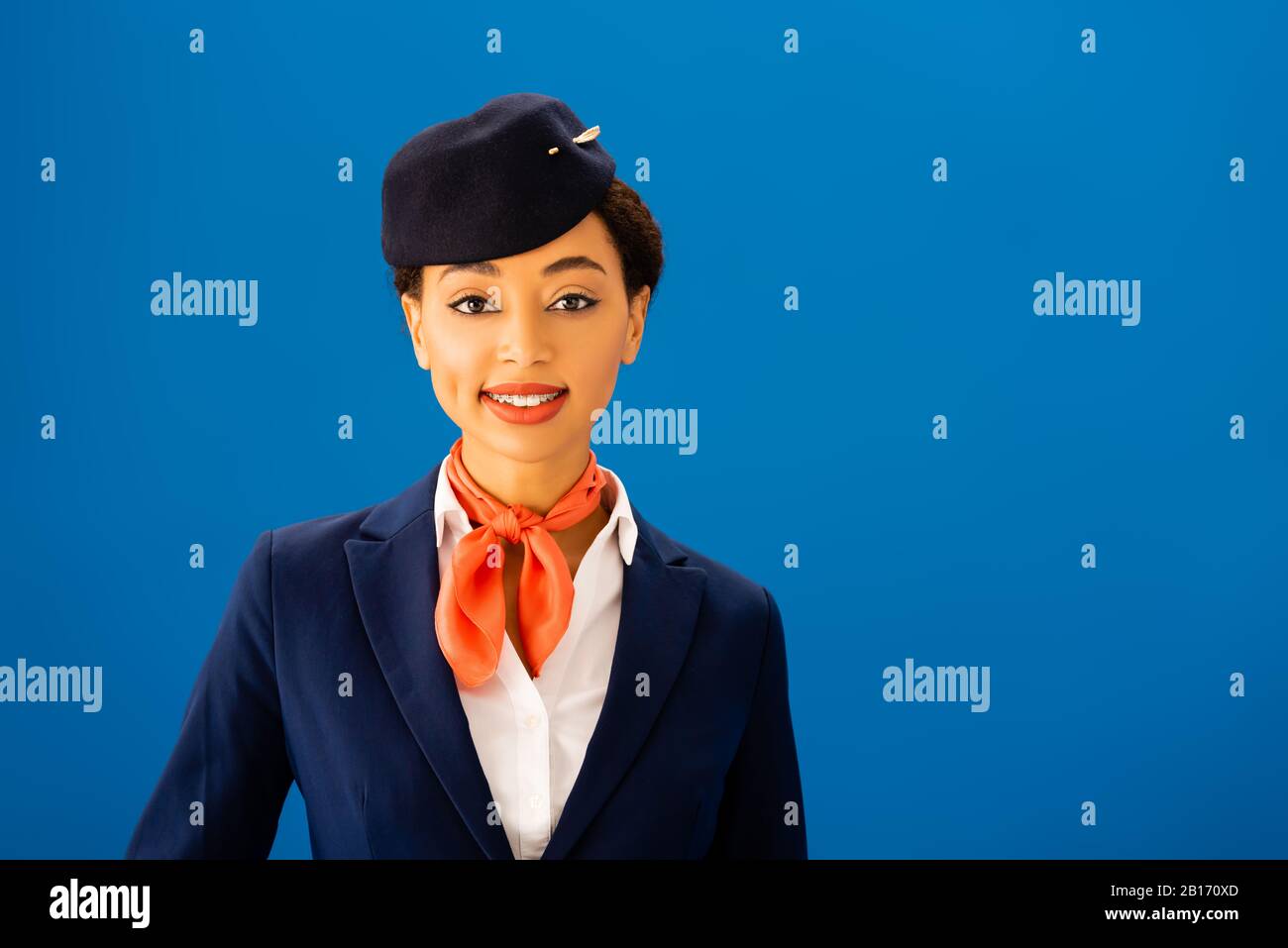 smiling african american flight attendant looking at camera isolated on blue Stock Photo