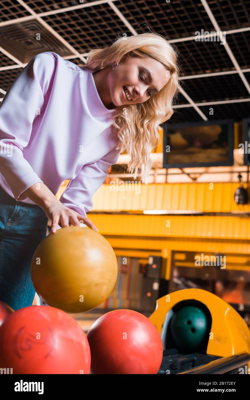 cheerful blonde girl taking bowling ball in bowling club Stock Photo