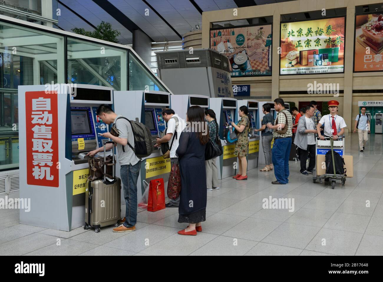 Passengers queue to buy tickets for high speed trains at the ticket machines in the waiting hall at Beijing South railway station, Beijing, China Stock Photo