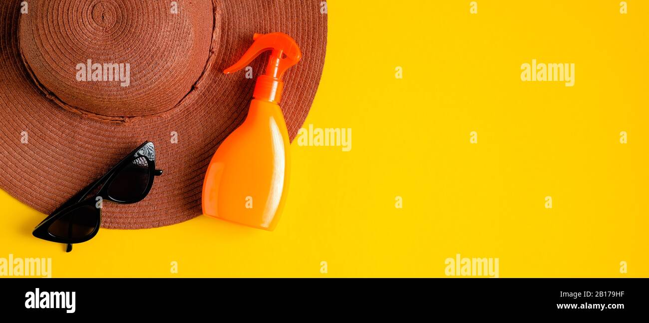 Sunblock spray in orange bottle without labels, beach hat and sunglasses on yellow background. Flat lay, top view. Beauty blog banner design with summ Stock Photo