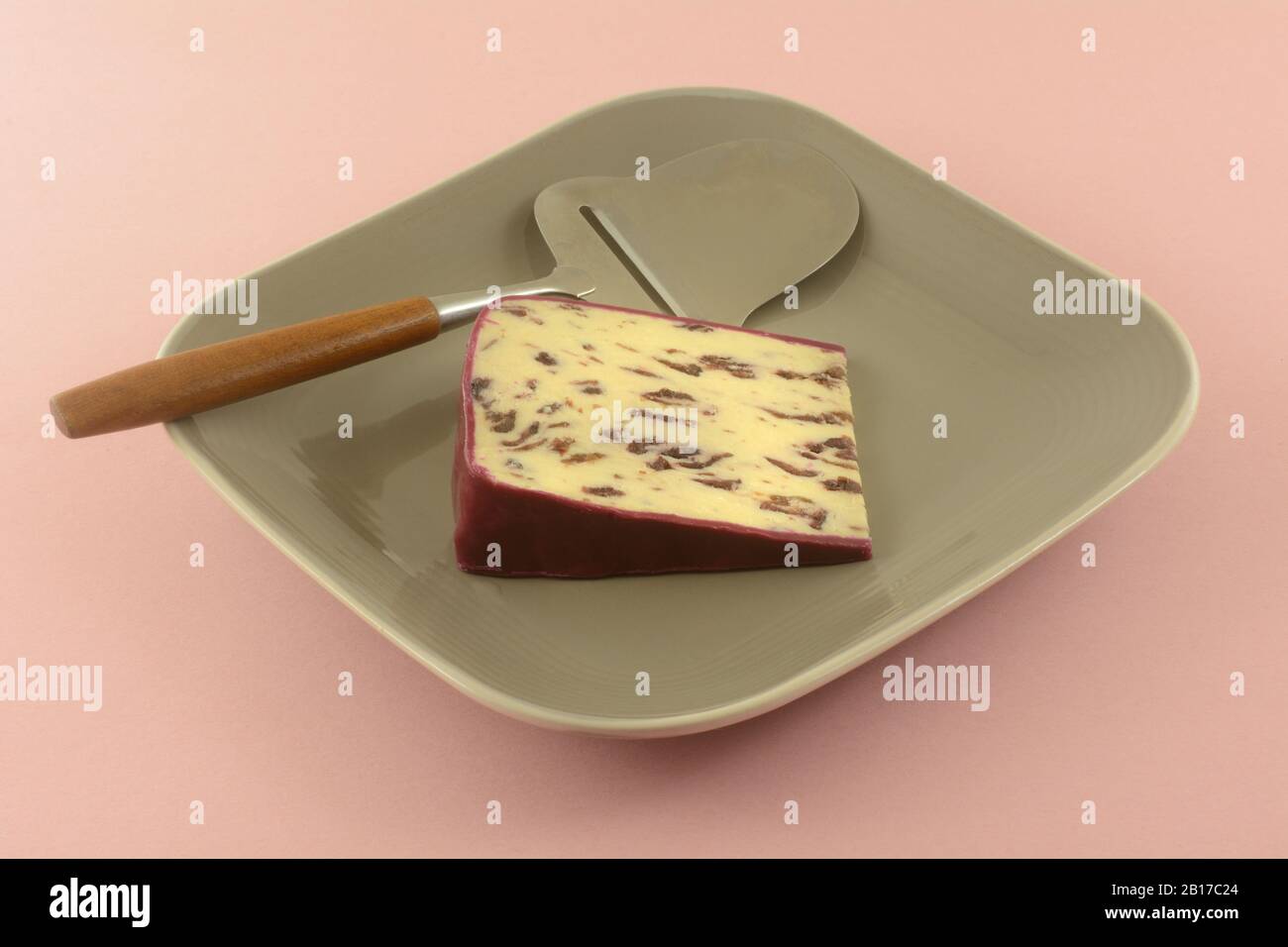 Slice of Wensleydale cranberry cheese with wax edges on plate with cheese slicer on pink background Stock Photo