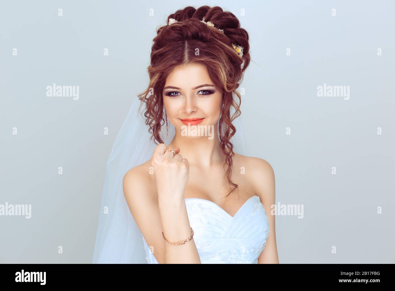 Angry spouse. Beautiful, pretty, smile woman in wedding dress girl, bride, lady  shows her hand with a fist. Isolated light blue background with copy Stock Photo