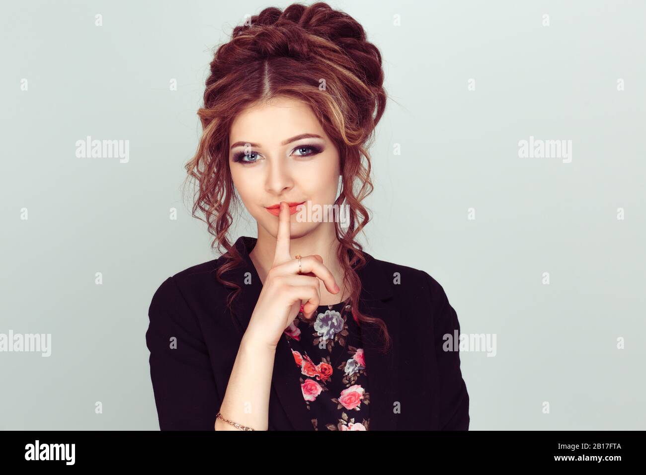 Shh. Woman asking for silence or secrecy with finger on lips hush hand gesture light green background wall. Pretty girl placing fingers on lips, shhh Stock Photo