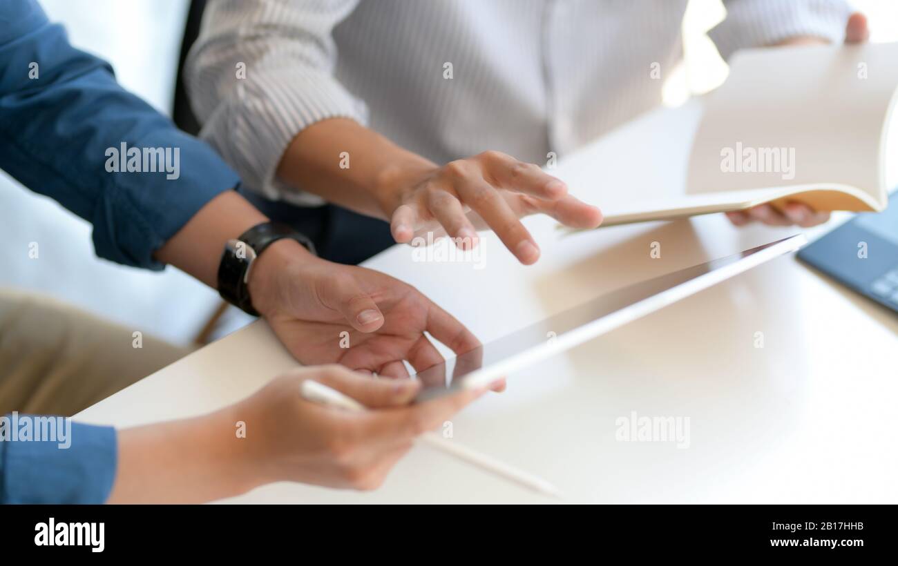 Close up view of two businesspeople consulting on their work with mock up tablet and notebook on white desk Stock Photo