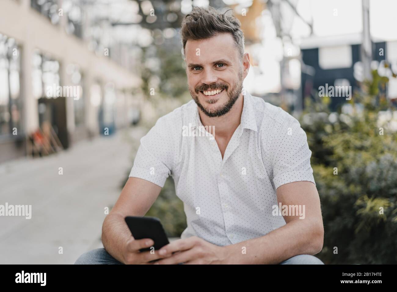 Young smiling man using smartphone and looking at camera Stock Photo