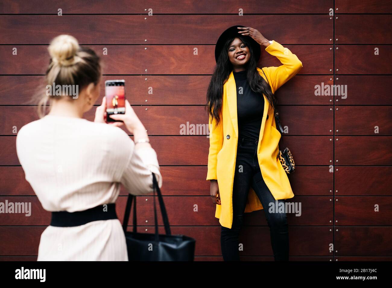 Smiling fashionable young woman posing for a photo at a wooden wall Stock Photo