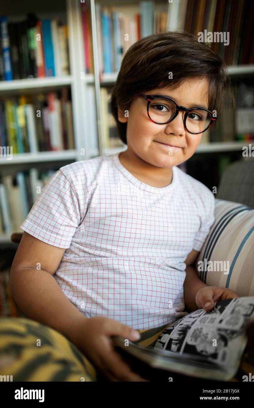 Portrait of smiling boy with glasses reading comic at home Stock Photo