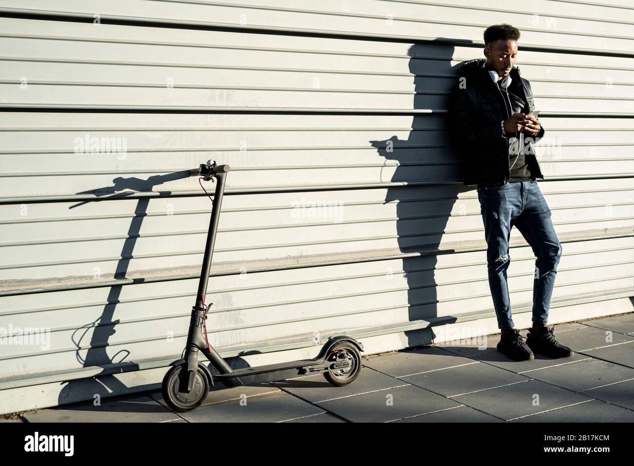 Man with smartphone and e-scooter outdoors Stock Photo