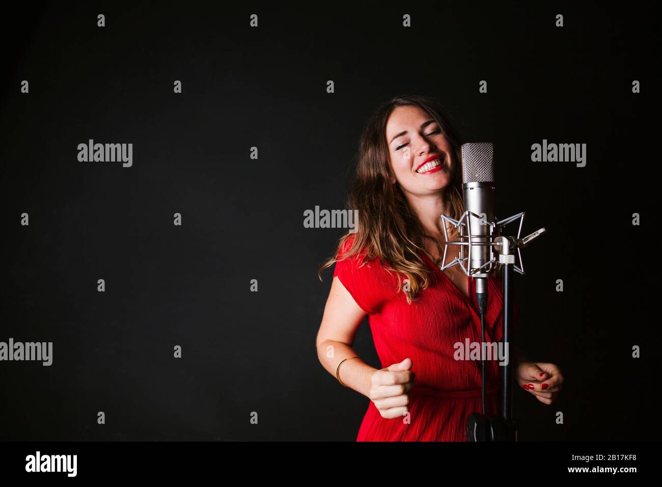 Portrait of female singer with microphone, wearing red dress Stock Photo