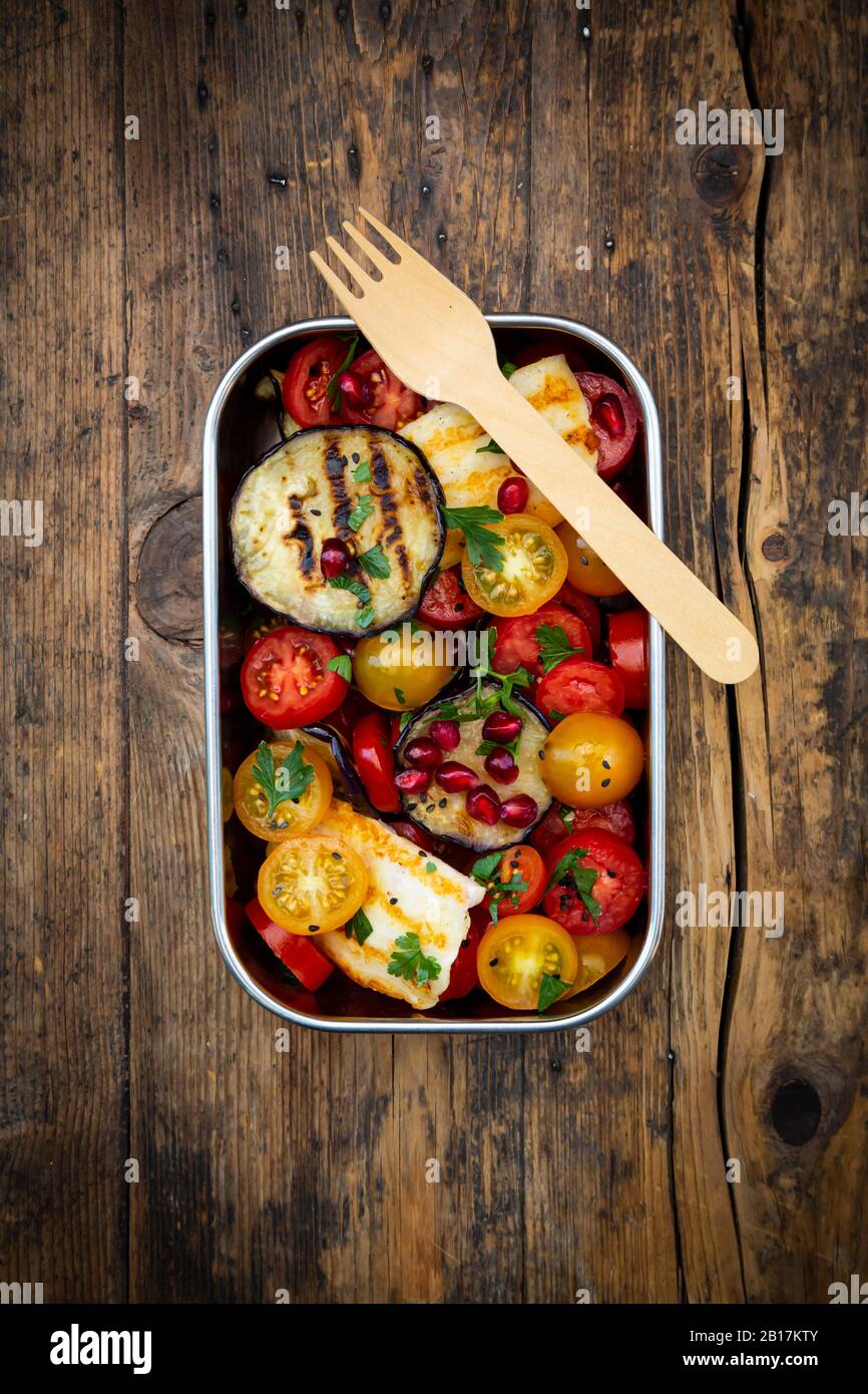 Lunch box with tomato salad with grilled vegetables and halloumi cheese, pomegranate seeds, sumac, black sesame and parsley Stock Photo