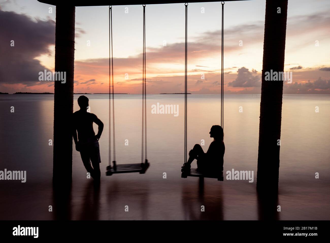 Couple on a swing at the sea at sunset, Maguhdhuvaa Island, Gaafu Dhaalu Atoll, Maldives Stock Photo