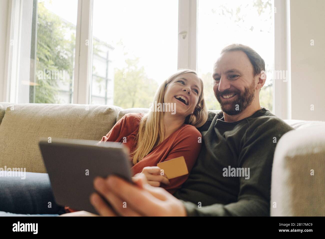 Couple sitting at home on couch, using digital tablet Stock Photo