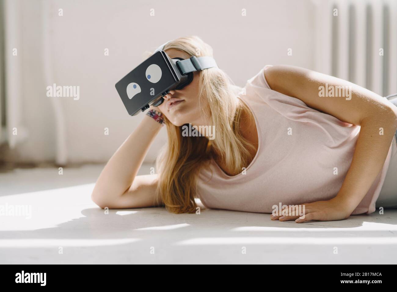 Young woman lying on the floor wearing VR glasses with squinting eyes Stock Photo