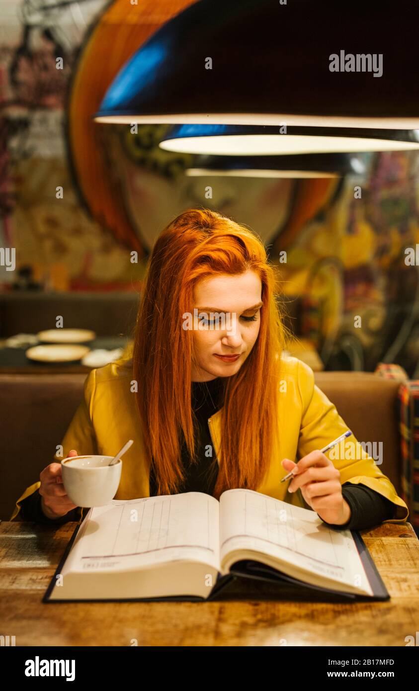 Portrait of redheaded young woman with book drinking coffee in a pub Stock Photo