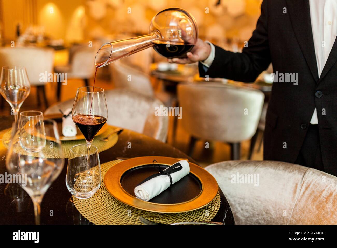 Waiter pouring wine from decanter into glass in fancy restaurant Stock Photo