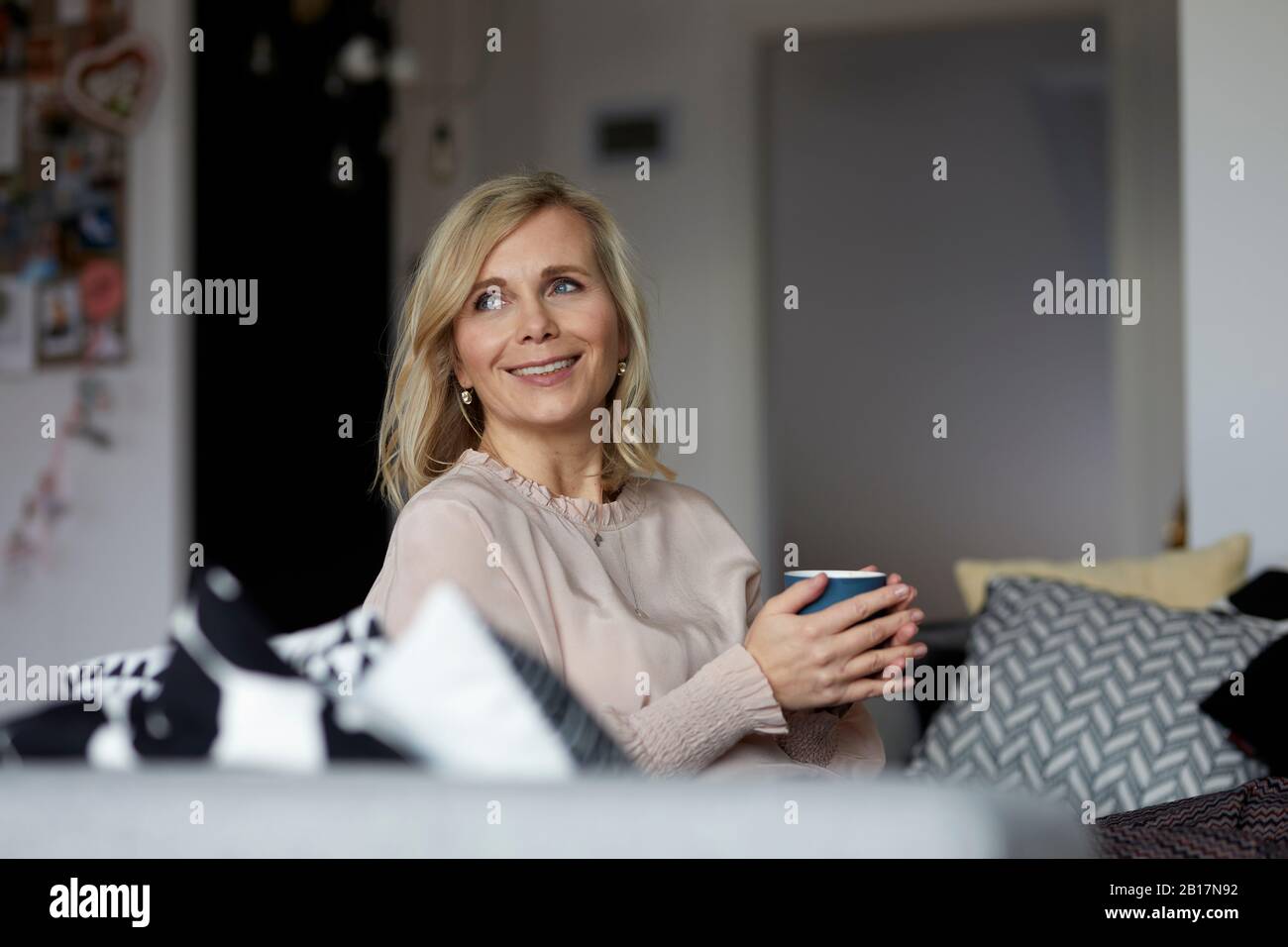 Smiling blond woman relaxing at home sitting on couch Stock Photo