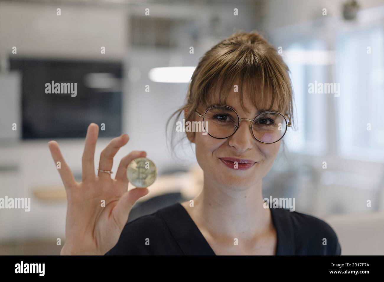 Portrait of businesswoman holding bitcoin in office Stock Photo