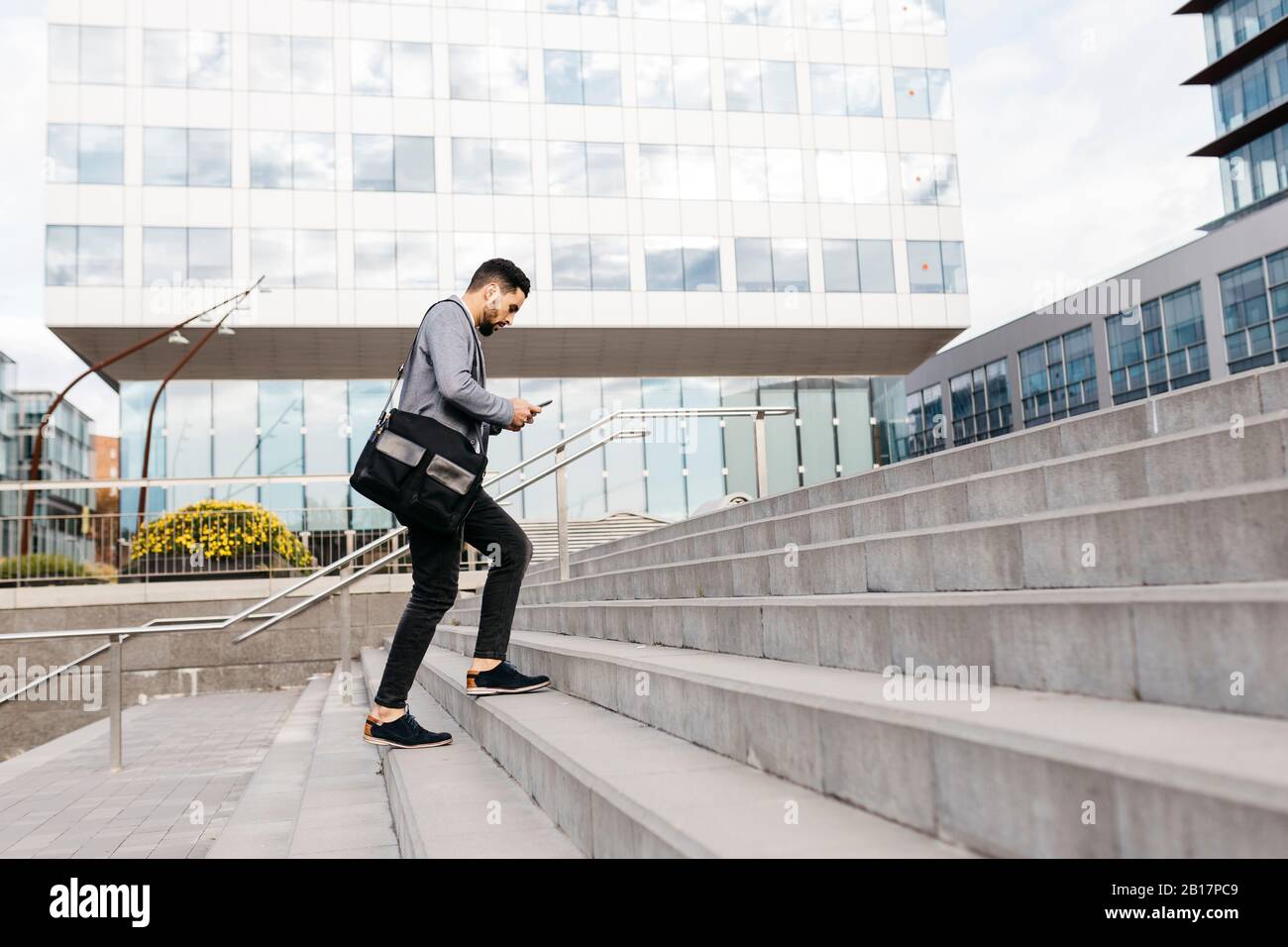 Casual young businessman using cell phone in the city walking up stairs Stock Photo