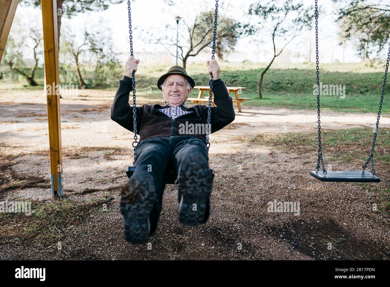 Old man swinging on playground in park Stock Photo