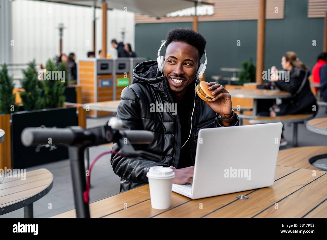 Man using laptop and eating a burger in a cafe Stock Photo