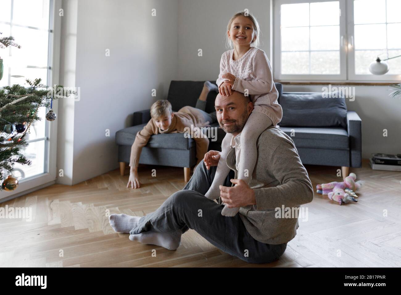 Portrait of mature man sitting on the floor at home playing with his little daughter Stock Photo
