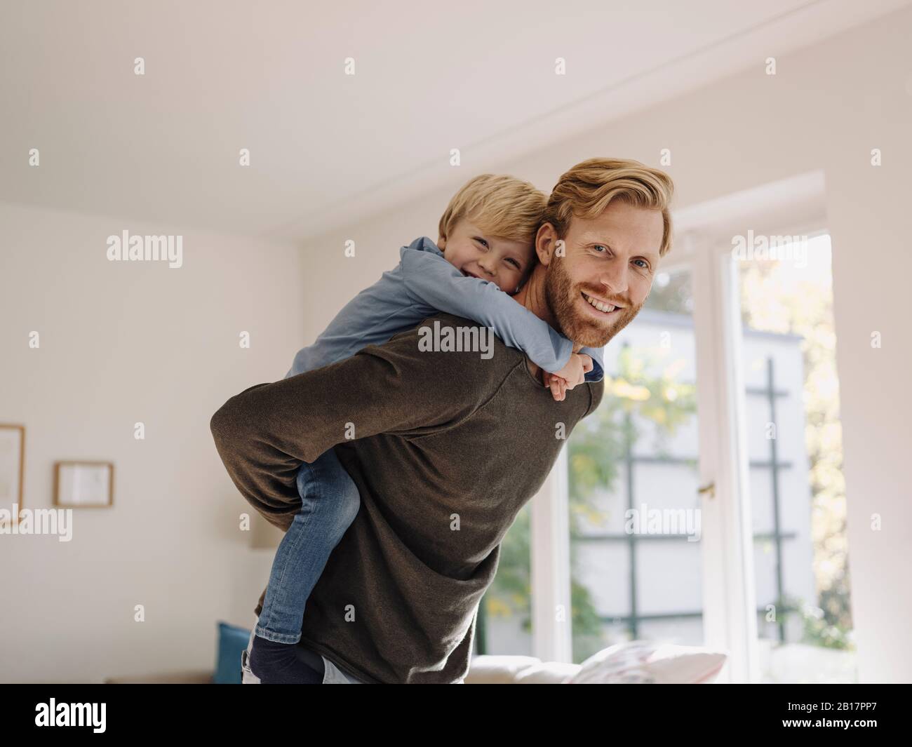 Portrait of happy father carrying son piggyback at home Stock Photo
