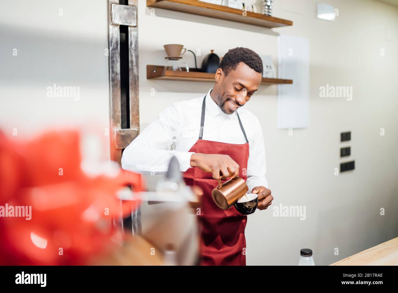 Smiling barista pouring milk froth into cup in a coffee shop Stock Photo