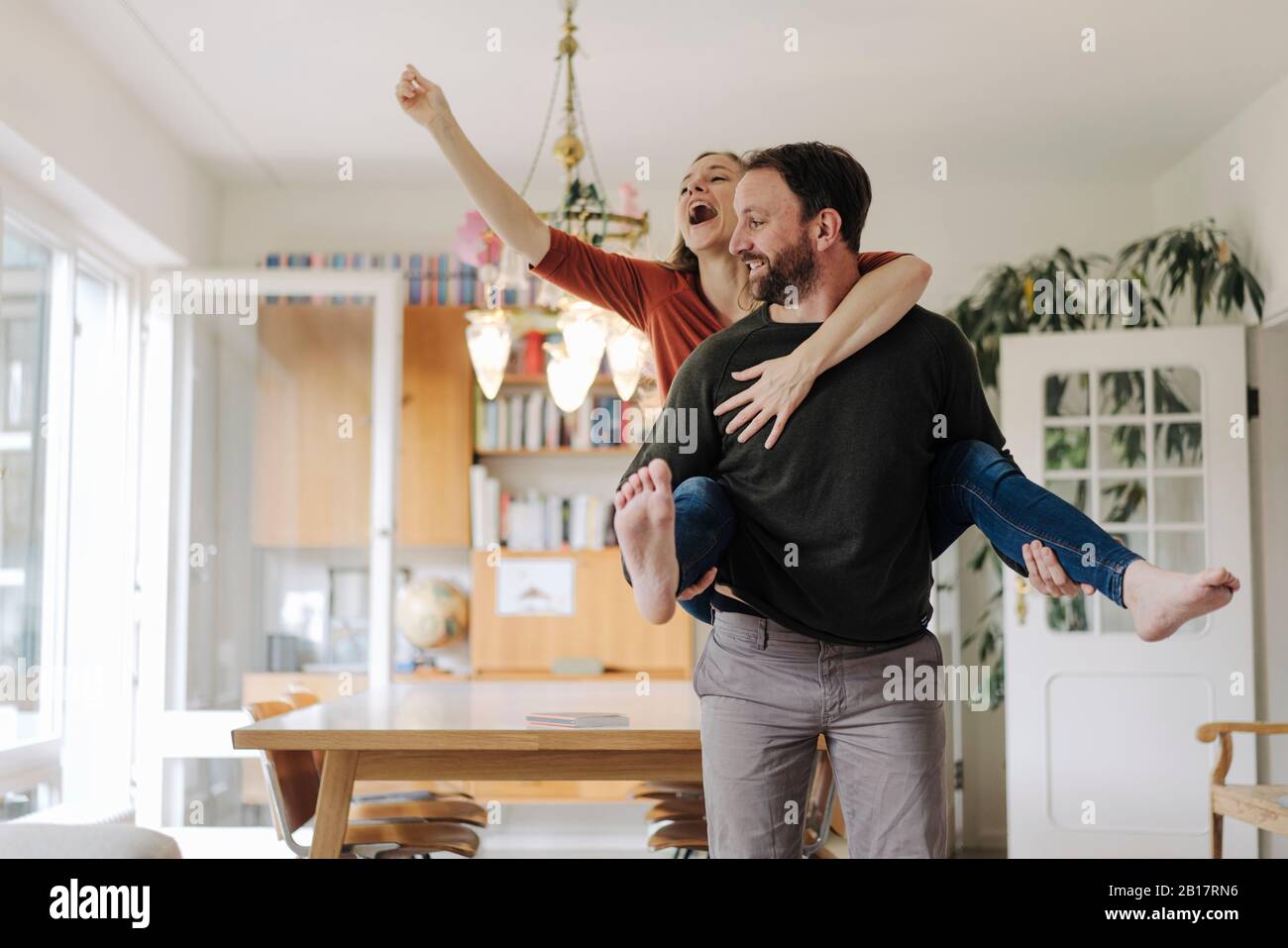 Man carrying happy woman piggyback in their comfortable home Stock Photo