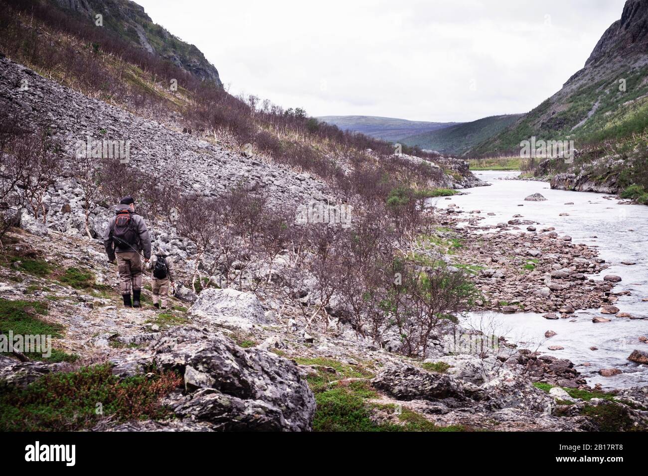 Fly fishermen hiking along river bank with mountains, Lakselv, Norway Stock Photo