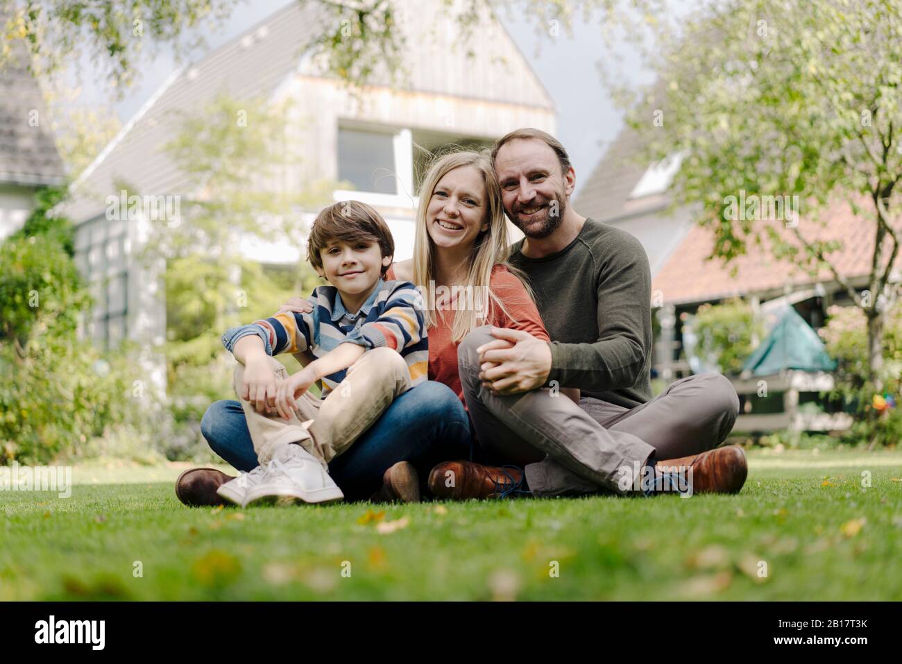 Happy family sitting on grass in their garden Stock Photo - Alamy