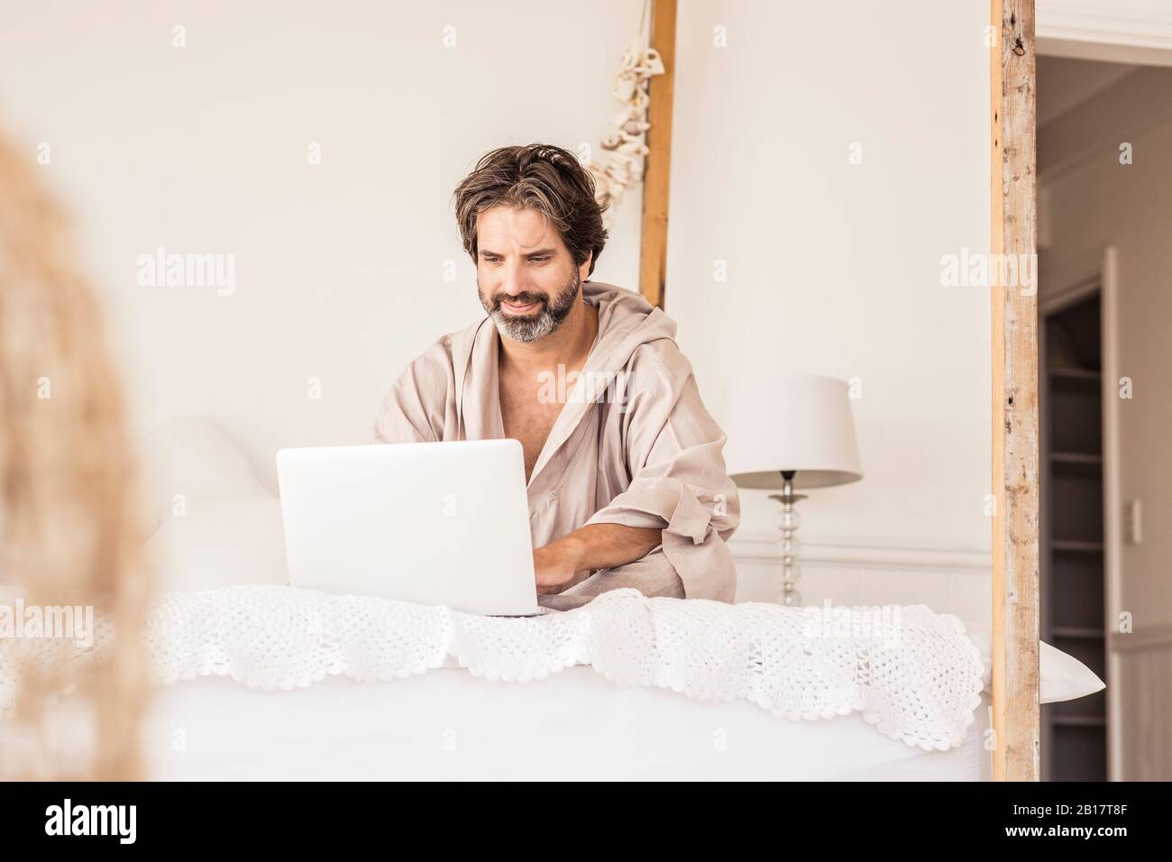Man wearing bathrobe and sitting on bed in bedroom Stock Photo