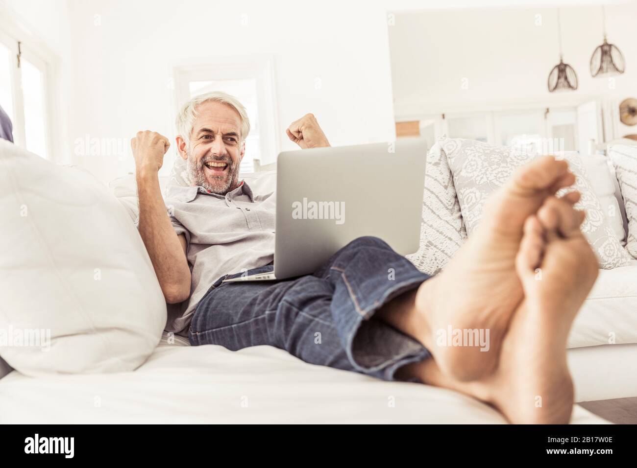 Mature man with laptop cheering on couch at home Stock Photo