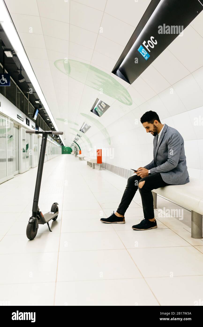 Young businessman with electric scooter and cell phone waiting in subway station Stock Photo
