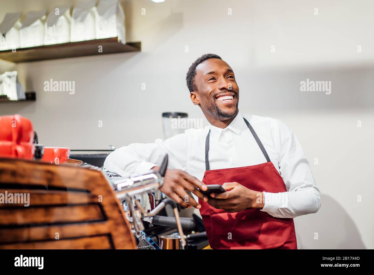 Happy barista holding cell phone in a coffee shop Stock Photo