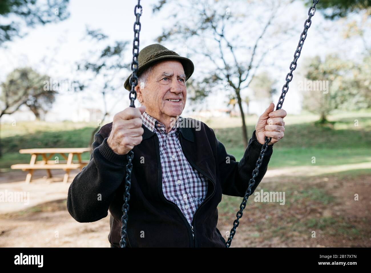 Old man swinging on playground in park Stock Photo
