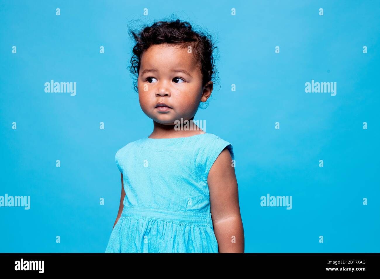 Portrait of little girl wearing light blue dress against blue